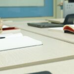 物件管理 Close-up of a professional meeting setup with hands, laptops, and notebooks on a wooden desk.