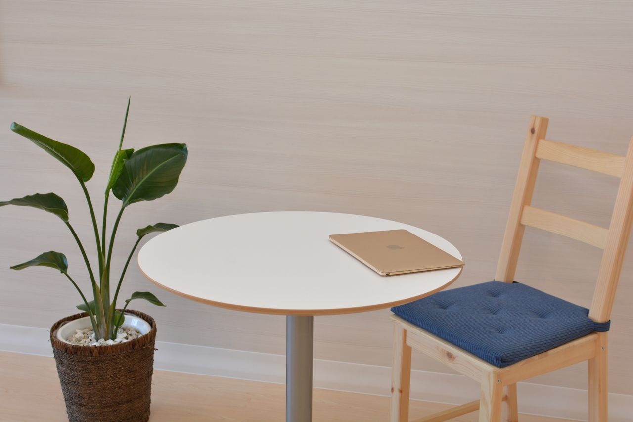 物件管理 A sleek minimalist office space featuring a table with a laptop and a potted indoor plant beside a wooden chair.